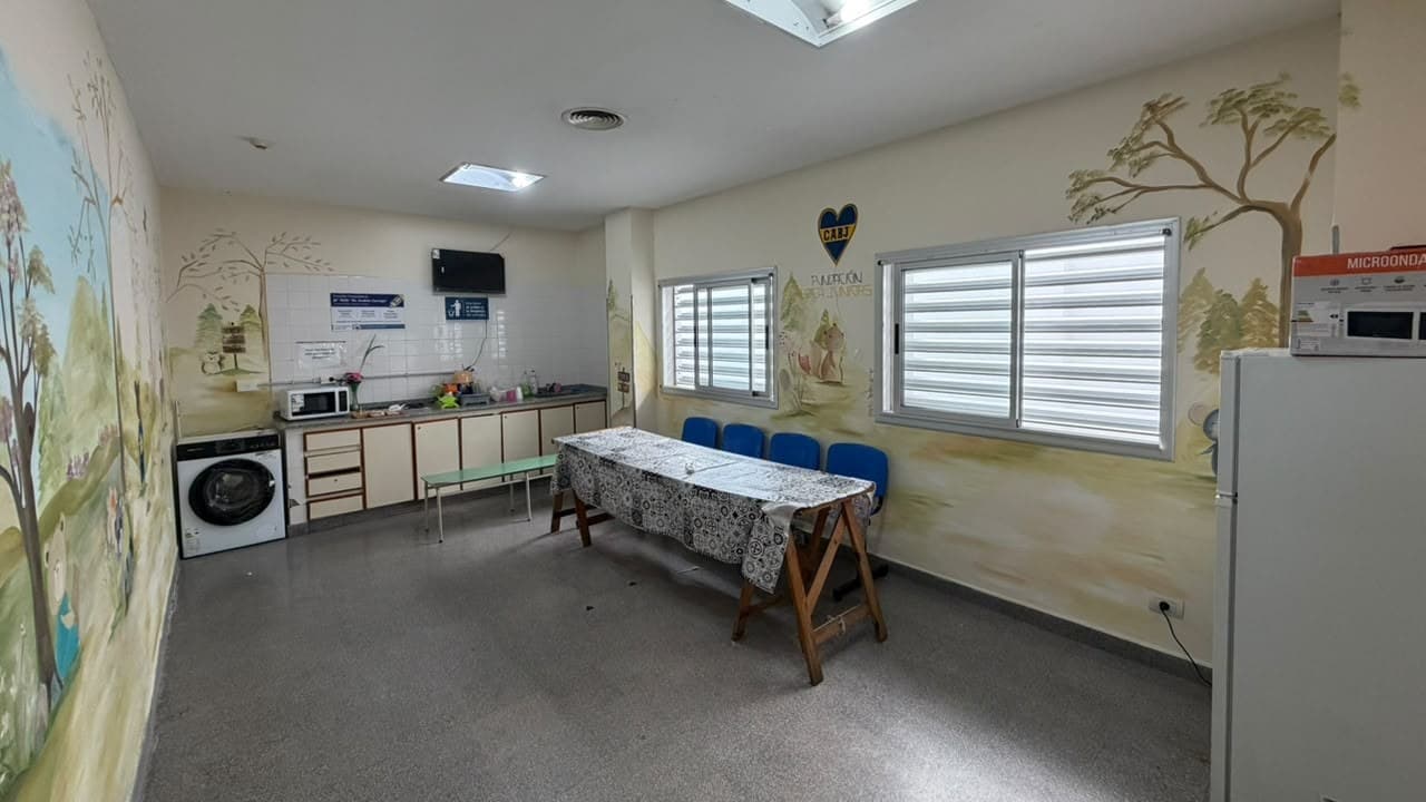 Estar de padres renovado, con las paredes pintadas con murales de árboles y animales, lavarropas, microondas, heladera y una mesa larga con sillas